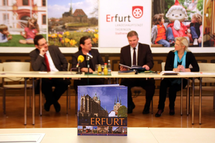 Der Erfurt-Bildband auf einem Tisch, im Hintergrund die Pressekonferenz zur Vorstellung der Neuerscheinung.