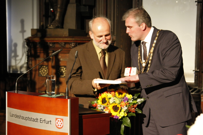 Foto: Tag der Deutschen Einheit © Stadtverwaltung Erfurt Im Rathausfestsaal stehen Festredner Mathias Ladstätter und Oberbürgermeister Andreas Bausewein (v.l.n.r.)neben dem Rednerpult. Herr Bausewein dankt Herrn Ladstätter mit Blumen und einem Buch.