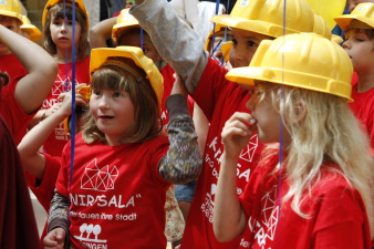 Foto - Kinder mit gelben Bauarbeiterhelmen bei der Eröffnung der Kinderstadt Knirpsala