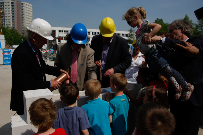Bauleute und Kinder befüllen einen Mauerstein