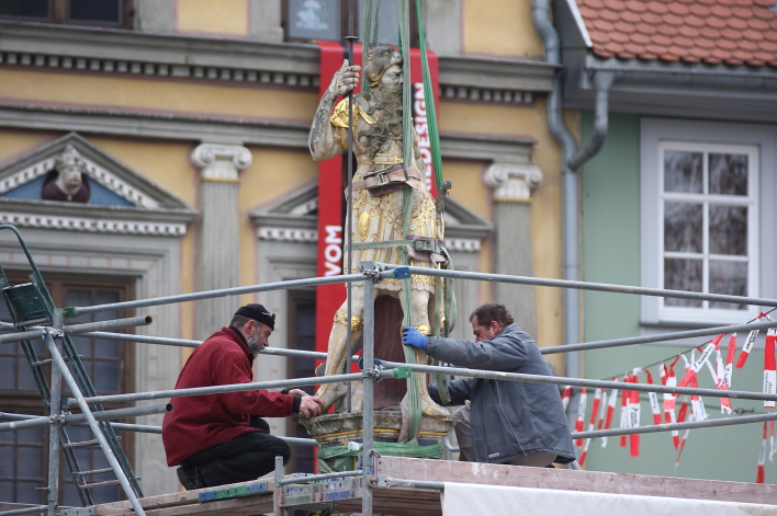 Zwei Arbeiter lockern eine am Kran hängende Römer-Statue vom Sockel.