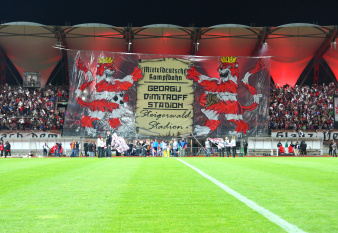 Zuschauer eines Fußballspiel entrollen ein großes Banner, auf dem die historischen Namen des Steigerwaldstadions aufgeführt sind.