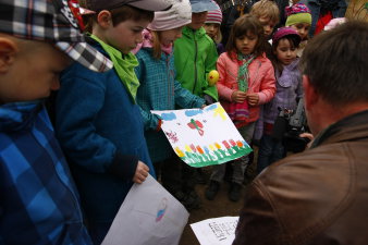 Eine Kindergruppe zeigt einem kniehenden Erwchsenen mehrere Bilder. 