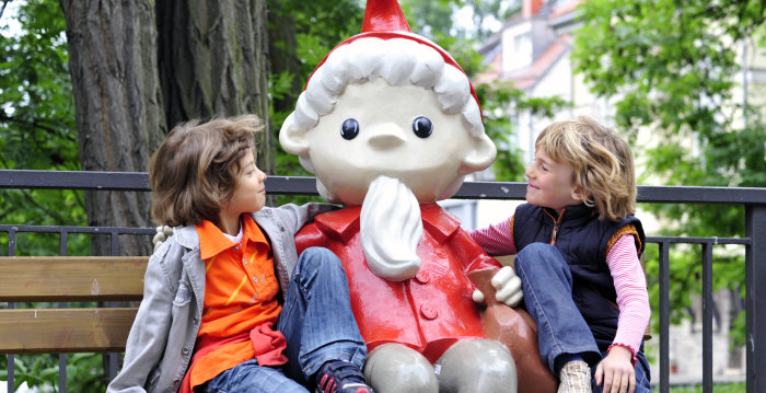 Foto: Sandmann-Figur auf der Rathausbrücke © Barbara Neumann Zwei Kinder sitzen mit der Sandmann-Figur auf einer Bank.