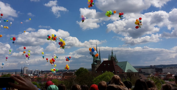 Vor dem Hintergrund des Erfurter Doms steigen Luftballontrauben mit daran befestigten Karten in den Himmel auf