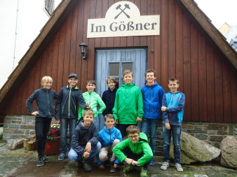 Zehn Schüler posieren im Freien vor einer Holzhütte, darauf das Schild mit dem Schriftzug "Im Gößner" unter zwei gekreuzten Hammern.