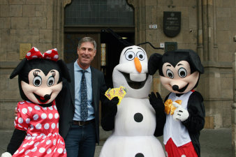 Drei als Disney-Figuren kostümierte Personen halten einen Fächer voller Freikarten in die Kamera. Dawischen eine männliche Person im Anzug.