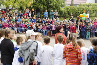 Mehrere hundert Grundschulkinder sitzen und stehen im Kreis um eine Frau mit Mikrofon. 