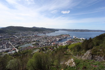 Blick auf die Hafenstadt Bergen, man sieht den Hafen und die sich vom Hafen ausbreitende Stadt und das ebenso felsige wie grüne Umland. 