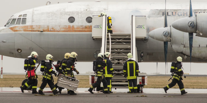 Einsatzkräfte der Feuerwehr stehen vor einem Flugzeug, aus dem es qualmt