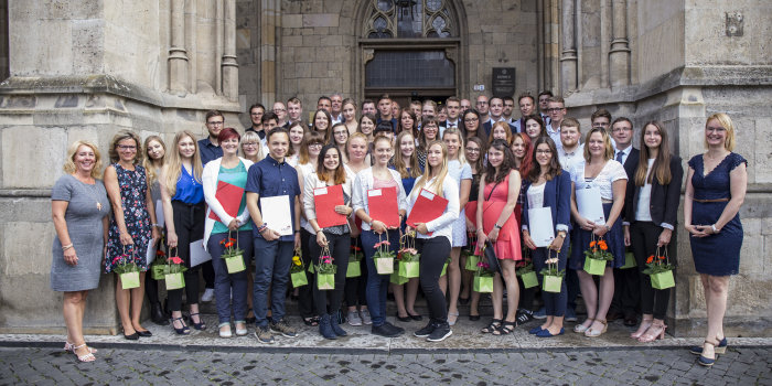 Eine Gruppe von mehr als 50 Jugendlichen und jungen Erwachsenen steht auf schmalen Treppen aufgereiht zwischen und vor einem historischen Bauwerk, dem Rathaus der Stadt Erfurt.