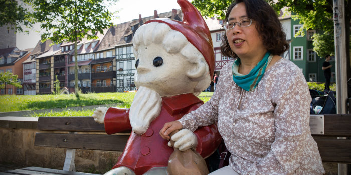 Luo Lingyan auf einer Parkbank neben der Sandmann-Figur