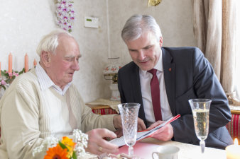 Der Oberbürgermeister und Rudi Keil schauen sich am Kaffeetisch Fotos des damaligen Profistehers an.