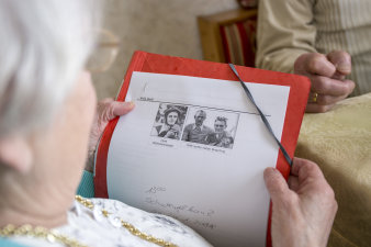 Abgedruckte Fotos von 1949 sind auf einem Blatt Papier abgedruckt und werden von einer älteren Dame in der Hand gehalten