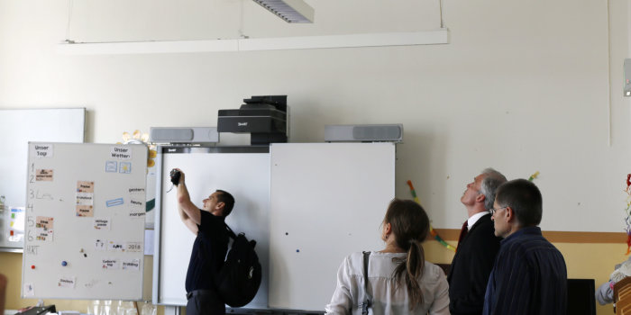 Drei Männer und eine Frau besichtigen einen Klassenraum einer Schule.