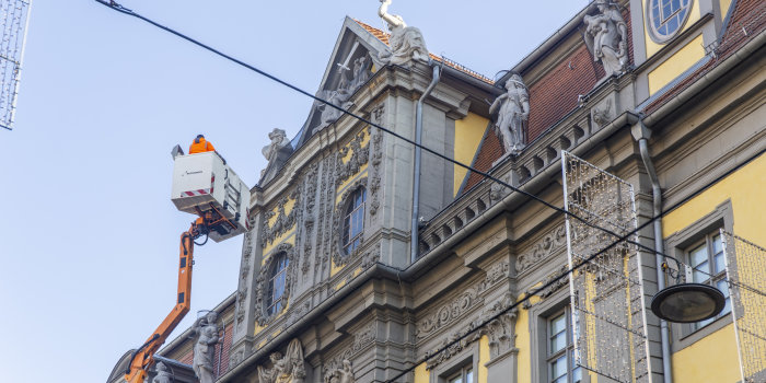 An der Fassade eines reich verzierten Gebäudes ist ein Hubsteiger mit einem Mann zu sehen. 