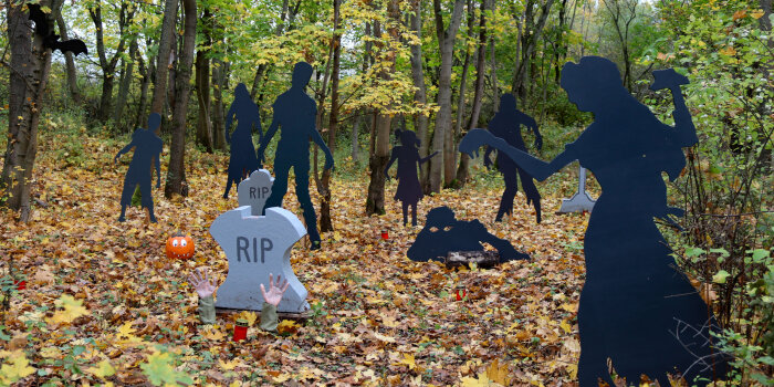Halloween-Deko in einem Wald mi einem Grabstein und lebensgroßen Figuren