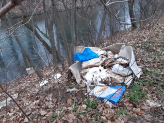verschiedener Müll, darunter ein Pizzakarton, an einer Böschung am Ufer eines Flusses