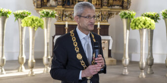 Ein Mann hält ein Mikrofon in der Hand und trägt eine große goldene Amtskette um den Hals.