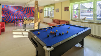 ein bunt gestalteter Raum mit Billiardtisch, Kicker und Tischtennisplatte