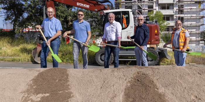 Fünf Männer stehen mit einer Schaufel vor einem Sandhaufen