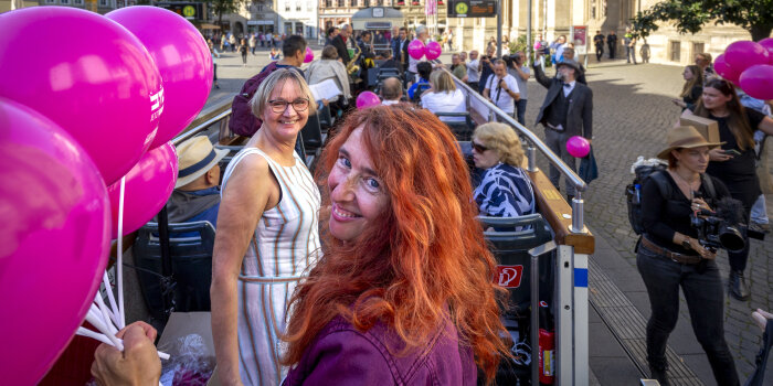 Zwei Frauen lächeln inmitten vieler Menschen. Eine Frau hält Luftballons in der Hand. 
