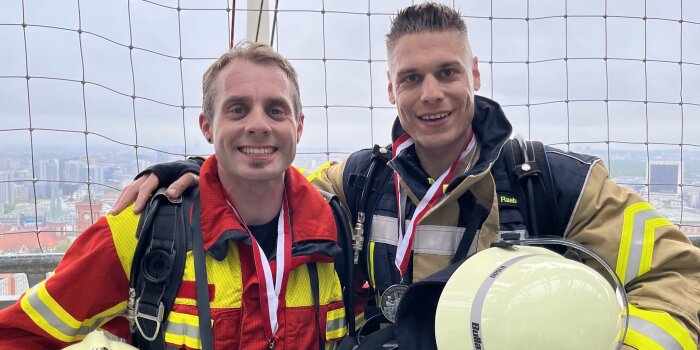 Zwei Männer in Feuerwehrkleidung stehen zusammen und lächeln. 
