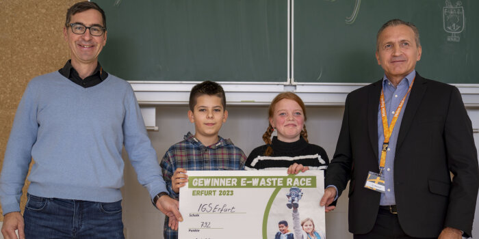 zwei Männer und zwei Kinder halten eine Tafel mit Aufschrift "Gewinner E-Waste Race"