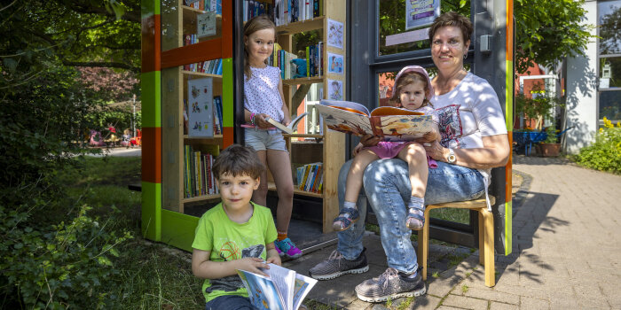 Eine Frau nutzt zusammen mit drei Kindern das Angebot einer Bücherzelle.