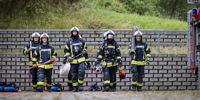 Sieben junge Männer in Feuerwehruniform laufen nebeneinander.