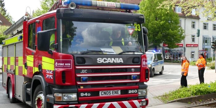 Ein britischer Feuerwehrwagen überquert in Begleitung eines Polizeiautos Straßenbahnschienen. 