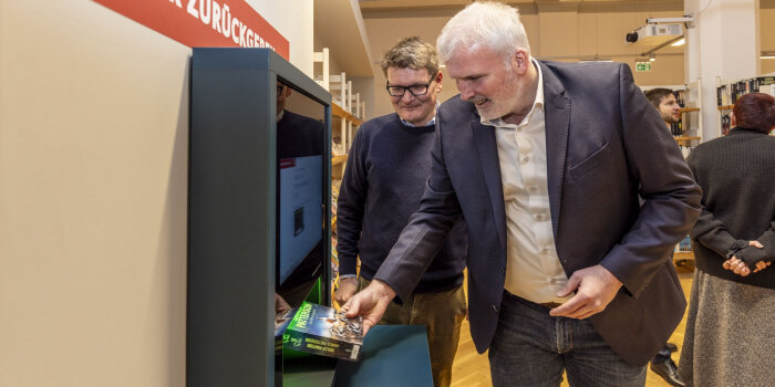 ein Mann legt ein Buch in einen Automaten