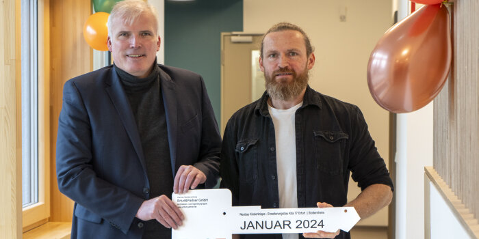 zwei Männer halten einen symbolischen Schlüssel mit Aufschrift "Januar 2024"