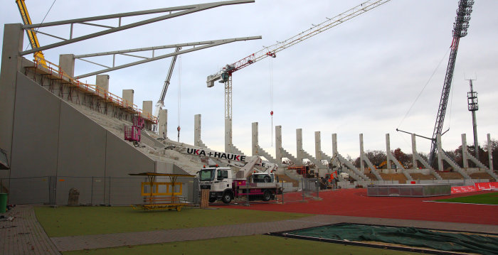Stadionbaustelle mit Kränen, mit deren Hilfe Dachträger einer Tribüne montiert werden.