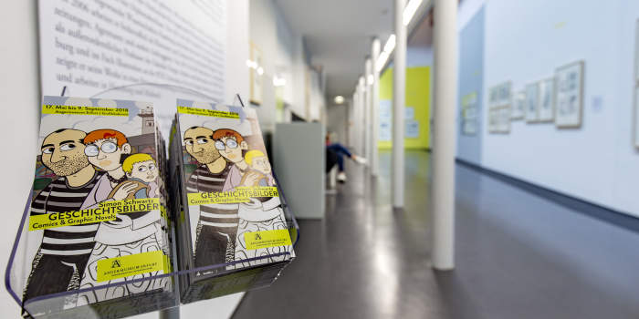 Im Vordergrund die Flyer, im Hintergrund ein Blick in den Raum