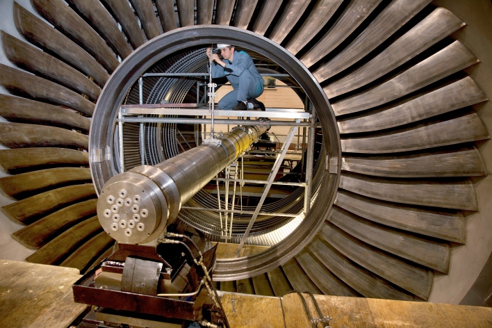 Picture: Generatorenbau © Siemens AG A worker kneeling on a scaffold inside a generator and mounting something.