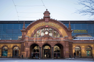 Eingangstor des Erfurter Hauptbahnhofes, zu dessen Seiten die Glasfronten der Zuggleise mit Werbepartner stehen; überall leichter Schnee.