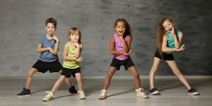 Vier Kinder posen in Sportklamotten vor einer grauen Wand. Sie sind wahrscheinlich in einem Tanzstudio.