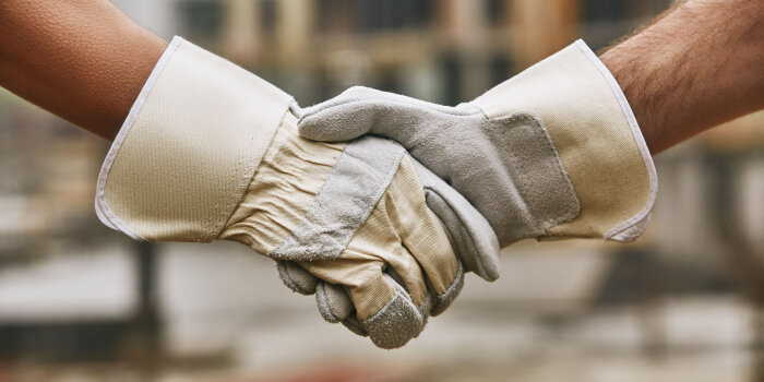 Zwei Hände in Schutzhandschuhen halten einander fest.