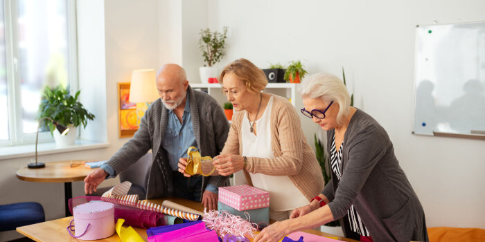 Drei ältere Personen packen Geschenke an einem Tisch ein.