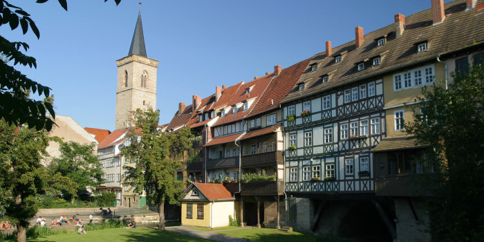 Mit Fachwerkhäusern bebaute Steinbrücke mit 6 Bögen sowie einer Kirche am Brückenende.