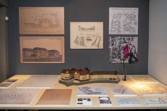 Blick in einer Ausstellung, auf dem Tisch und an der Wand befinden sich Pläne, in der Mitte ein Stadtmodell