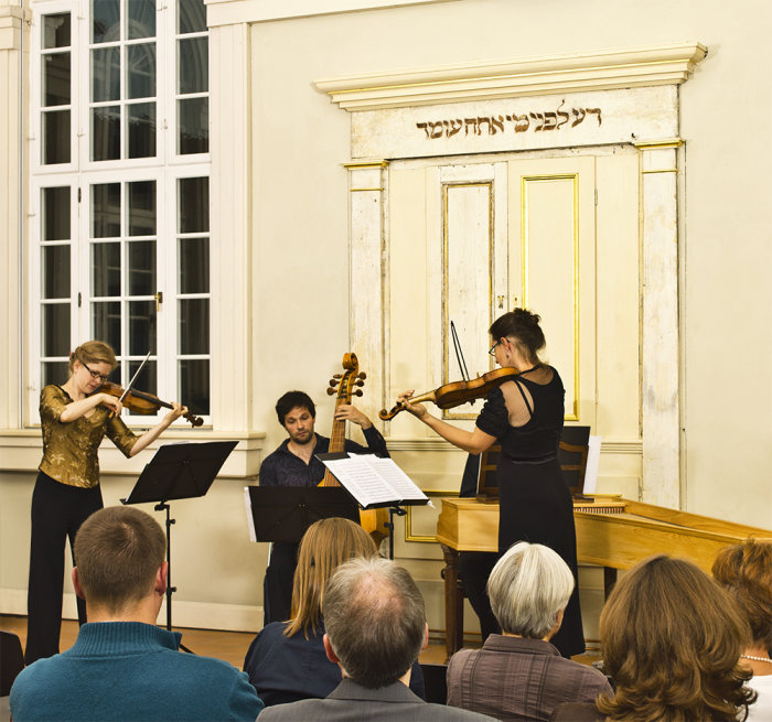 Musiker an Geige und Kontrabass. Im Vordergrund sitzt Publikum