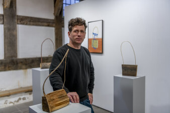 ein Mann steht zwischen drei handtaschenförmigen Holzskulpturen