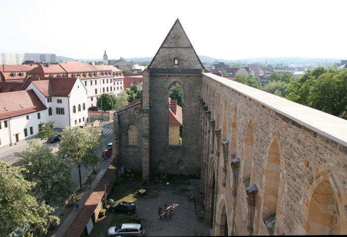 Blick auf die Ruine der Barfüßerkirche Blick auf die erhaltene Giebelseite der Kirche, die Wand die Hauptschiffes rechts im Bild. Dahinter die Stadt, unten, im ehemaligen Kirchenraum, Autos.