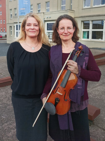 zwei Frauen stehen nebeneinander, eine hält eine Violine