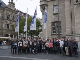 Das Bild zeigt die Teilnehmer der Impulsveranstaltung zur Umsetzung des Weltaktionsprogramms in Thüringen vor dem Erfurter Rathaus.Im Hintergrund die Flaggen zur BNE Weltdekade.