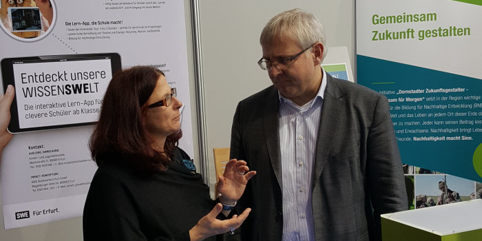 Foto: Am Unesco-Tag auf der Didacta wurde im Rahmen eines Expertengesprächs ein Blick auf das Thema BNE und lokales Engagement in Erfurt gerichtet. Rechts im Bild Josef Ahlke von der Stabsstelle Nachhaltigkeitsmanagement im Dezernat Wirtschaft und Umwelt der Landeshauptstadt © privat Ein Herr und eine Dame im Gespräch, im Hintergrund Informationstafeln
