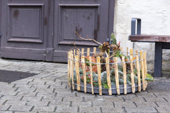 ein rundes, in einen niedrigen Holzzaun eingefasstes, weihnachtliches Arrangement