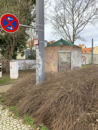 eine öffentliche WC-Anlage, davor eine Fläche mit braunen Sträuchern